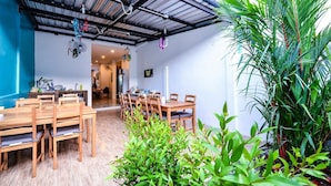 A dining area with wooden tables and chairs, a ceiling with exposed beams, and a large potted plant. - Two Color Patong (Patong)