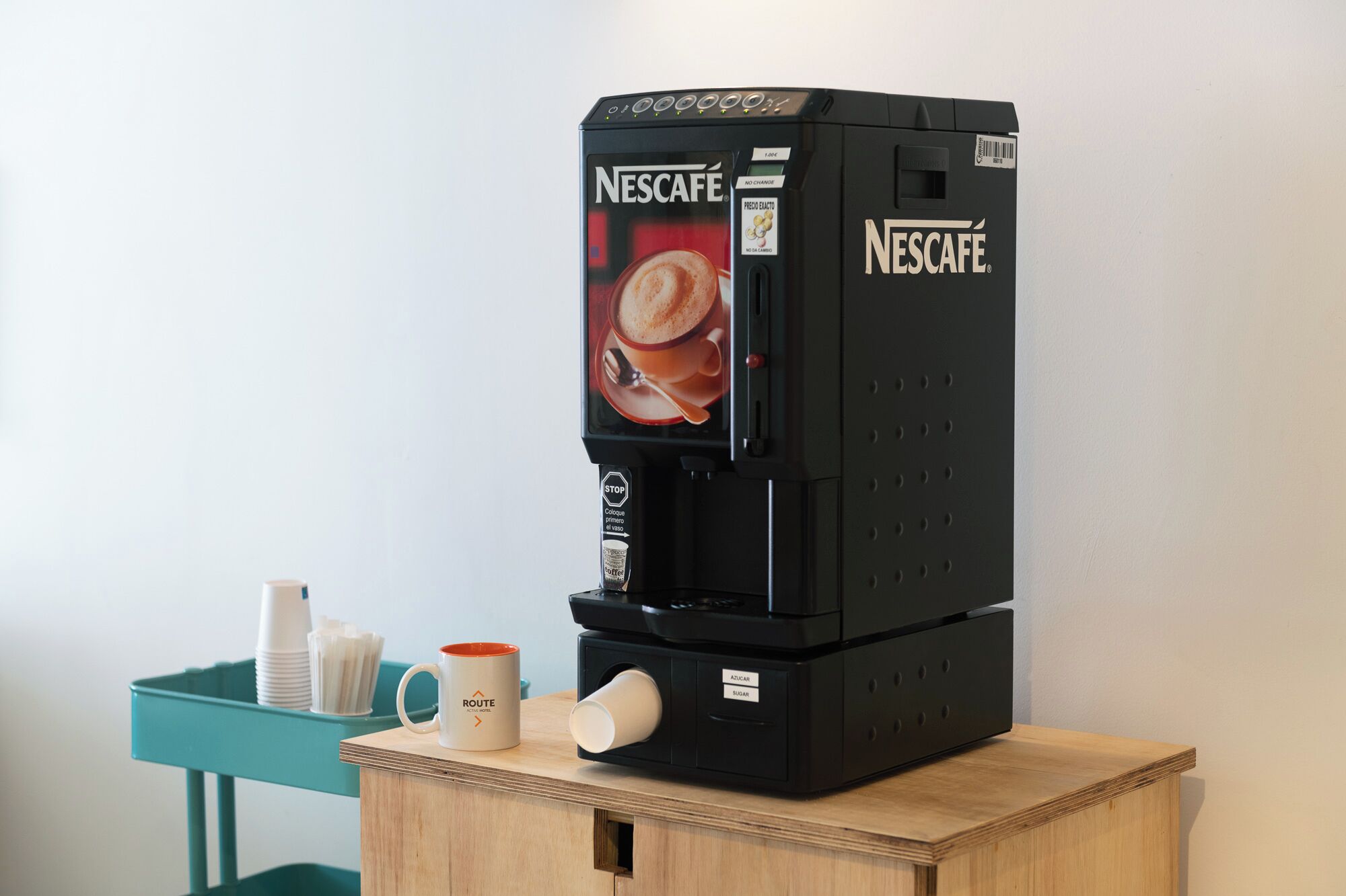A Nescafé coffee machine on a wooden table with a teal tray holding cups and a mug.