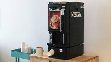 A Nescafé coffee machine on a wooden table with a teal tray holding cups and a mug.