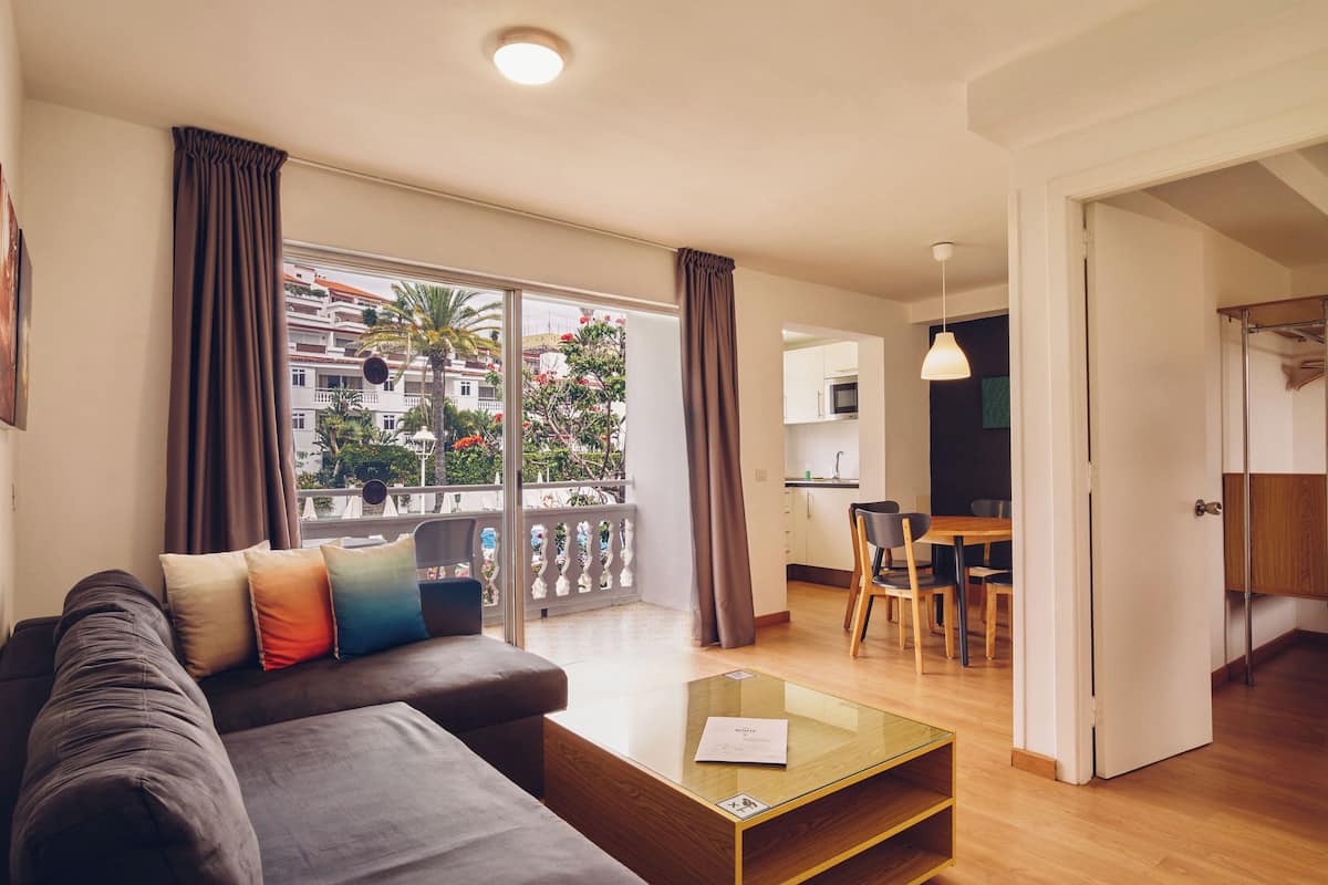 A modern living room with a sofa, a glass coffee table, and a view of a balcony with curtains.
