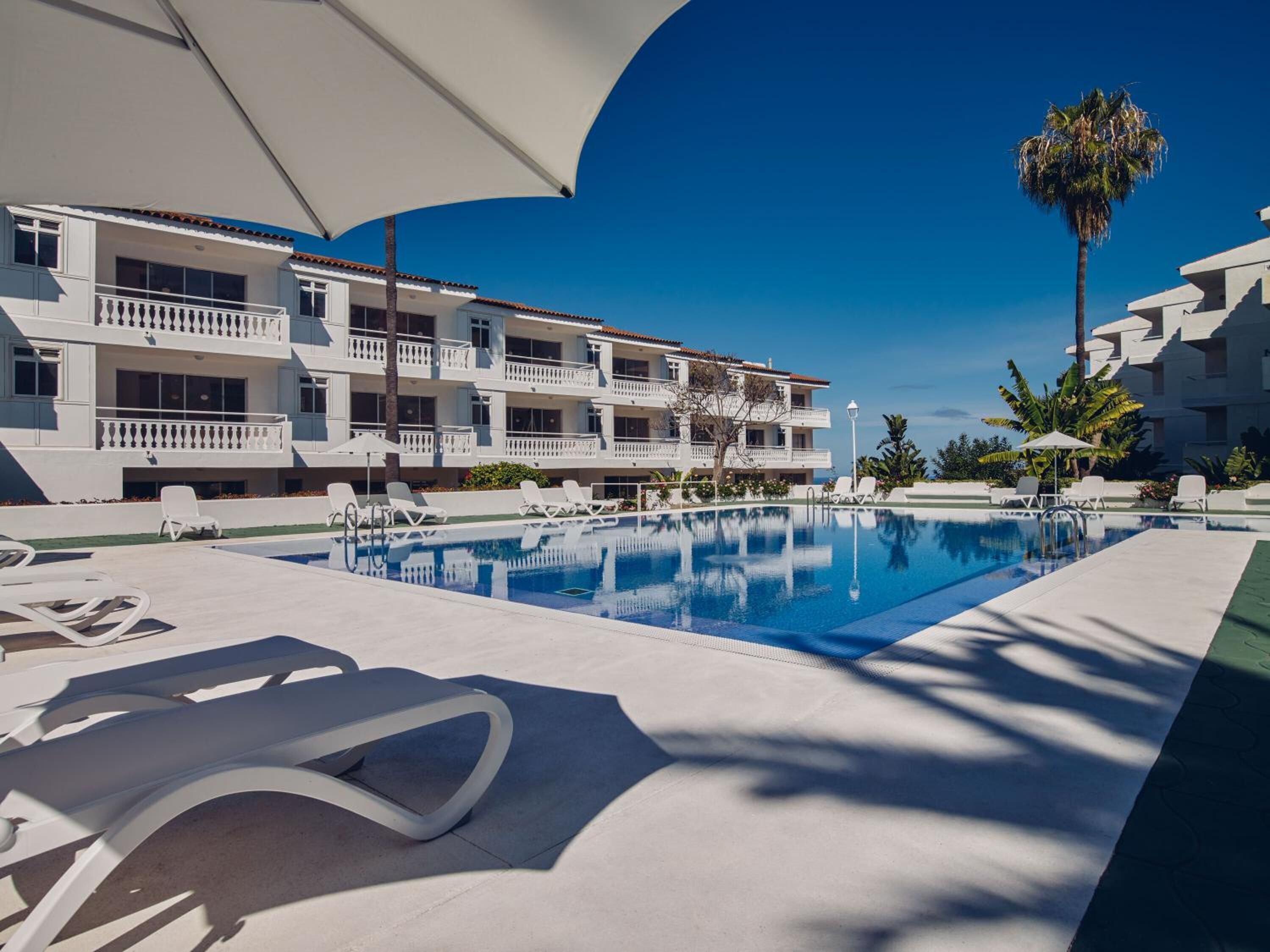 Un hôtel doté d’une piscine, de balcons blancs et de palmiers.