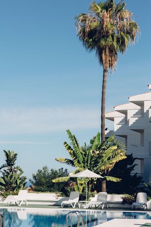 Una piscina al aire libre, sombrillas, sillones reclinables de piscina