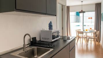 Una cocina moderna con pileta, microondas y tetera, un comedor con mesa y sillas, y vista al balcón exterior.