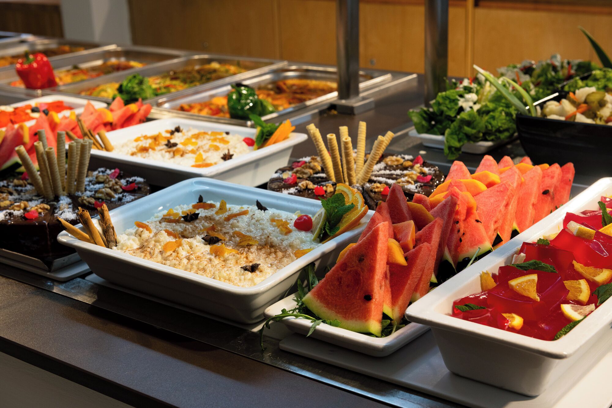 Ein reichhaltiges Buffet mit verschiedenen Speisen, darunter ein Reisgericht mit Orangen, Wassermelone und einem roten Fruchtsaft.