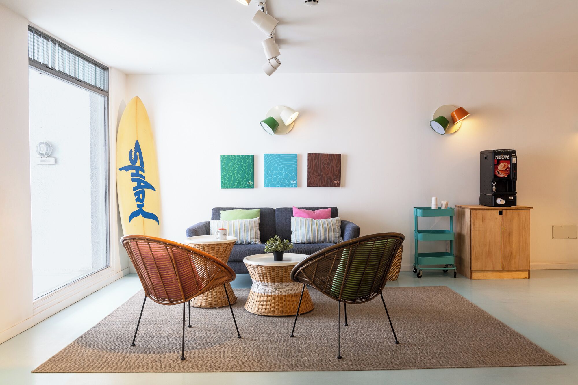 Una sala de estar moderna con un sofá, dos sillones de mimbre, una cafetera y una decoración con una tabla de surf.