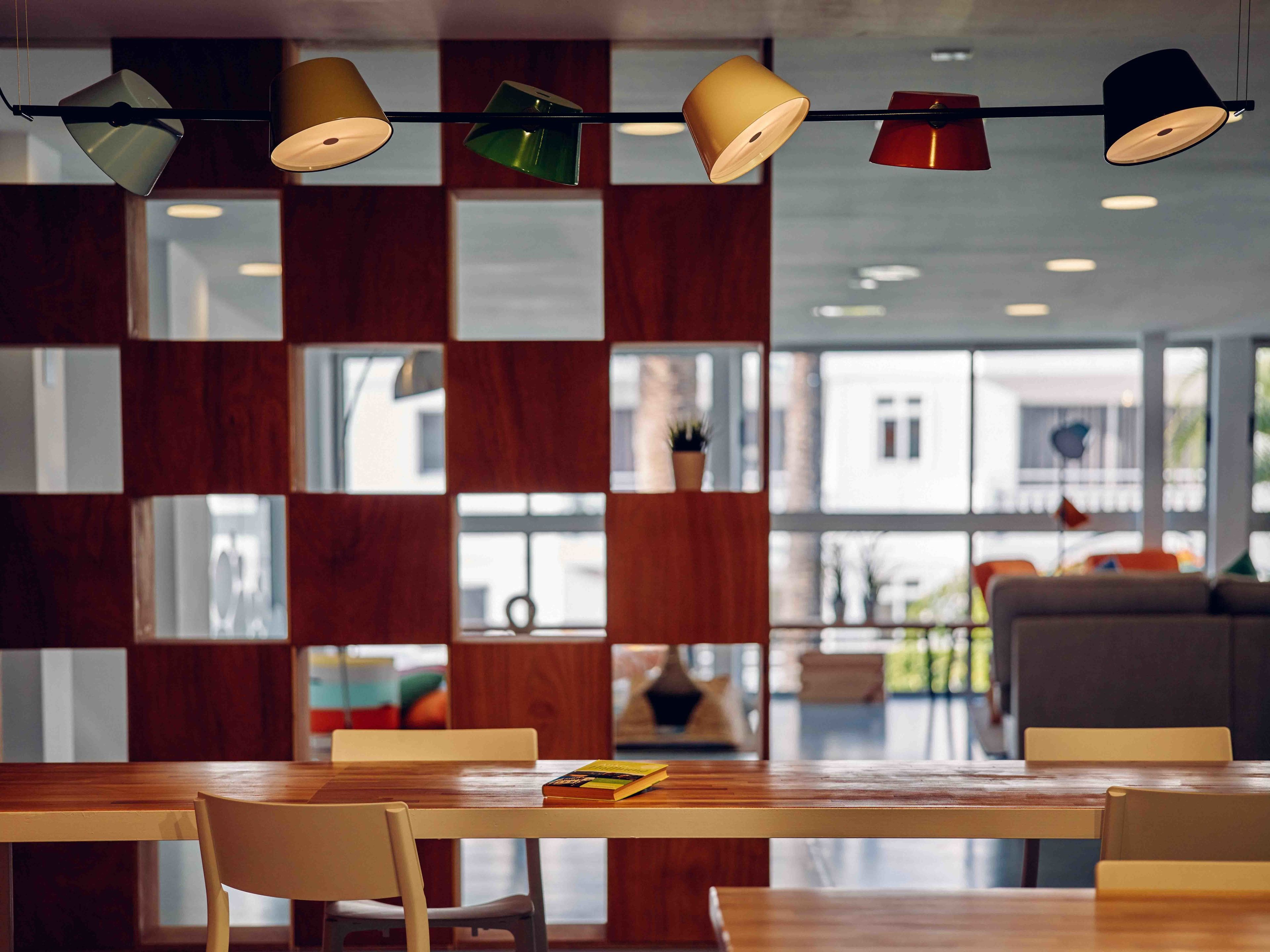 A modern dining area with wooden tables and chairs, a hanging light fixture, and a view of the outside through large windows.