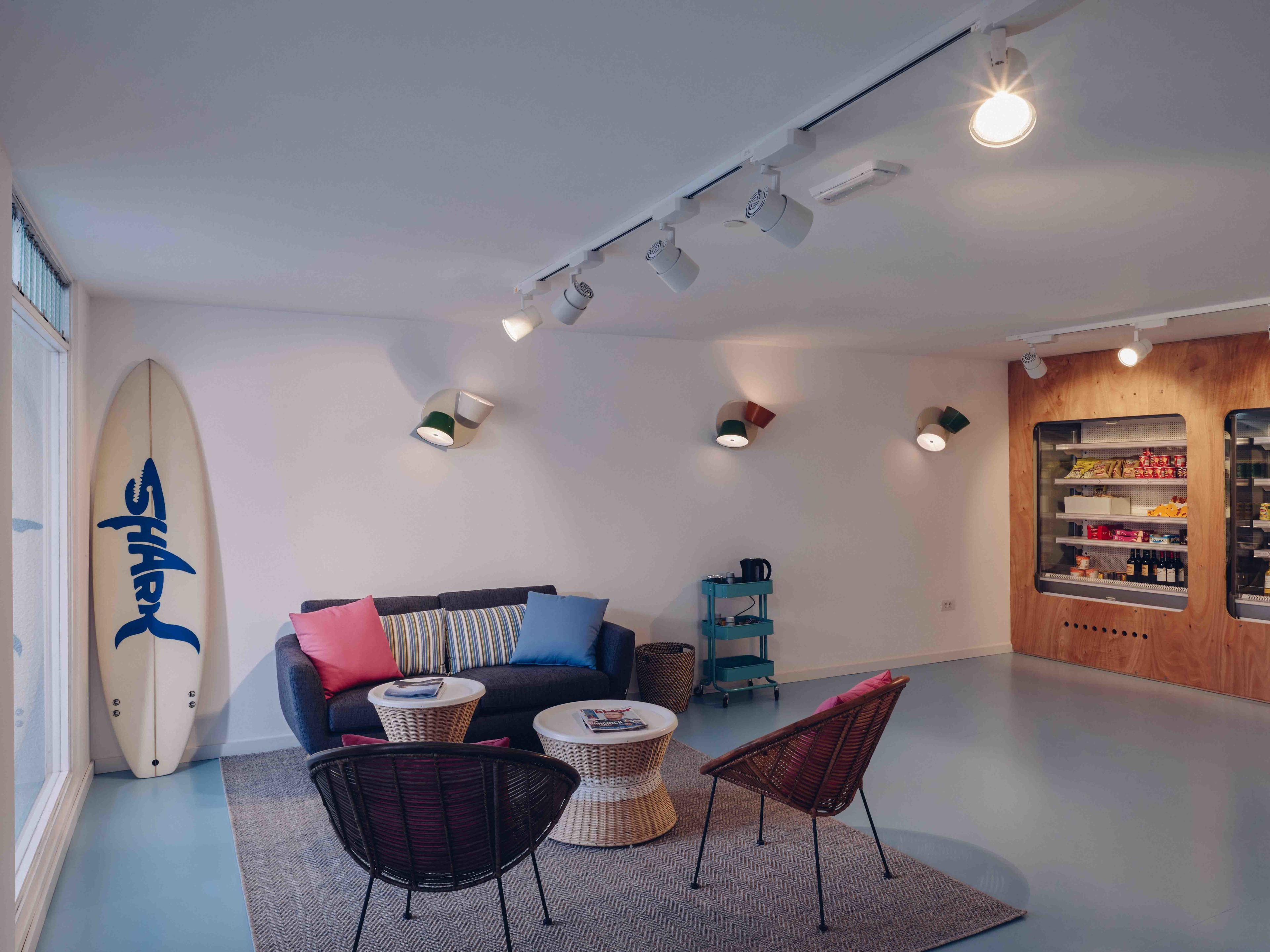 Una sala de estar moderna con un sofá, dos mesas redondas, una tabla de surf y un panel de madera con estantes.