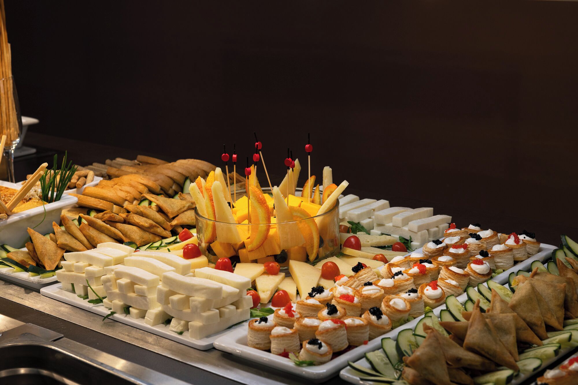 A buffet with various food items including cheese, fruits, and pastries.