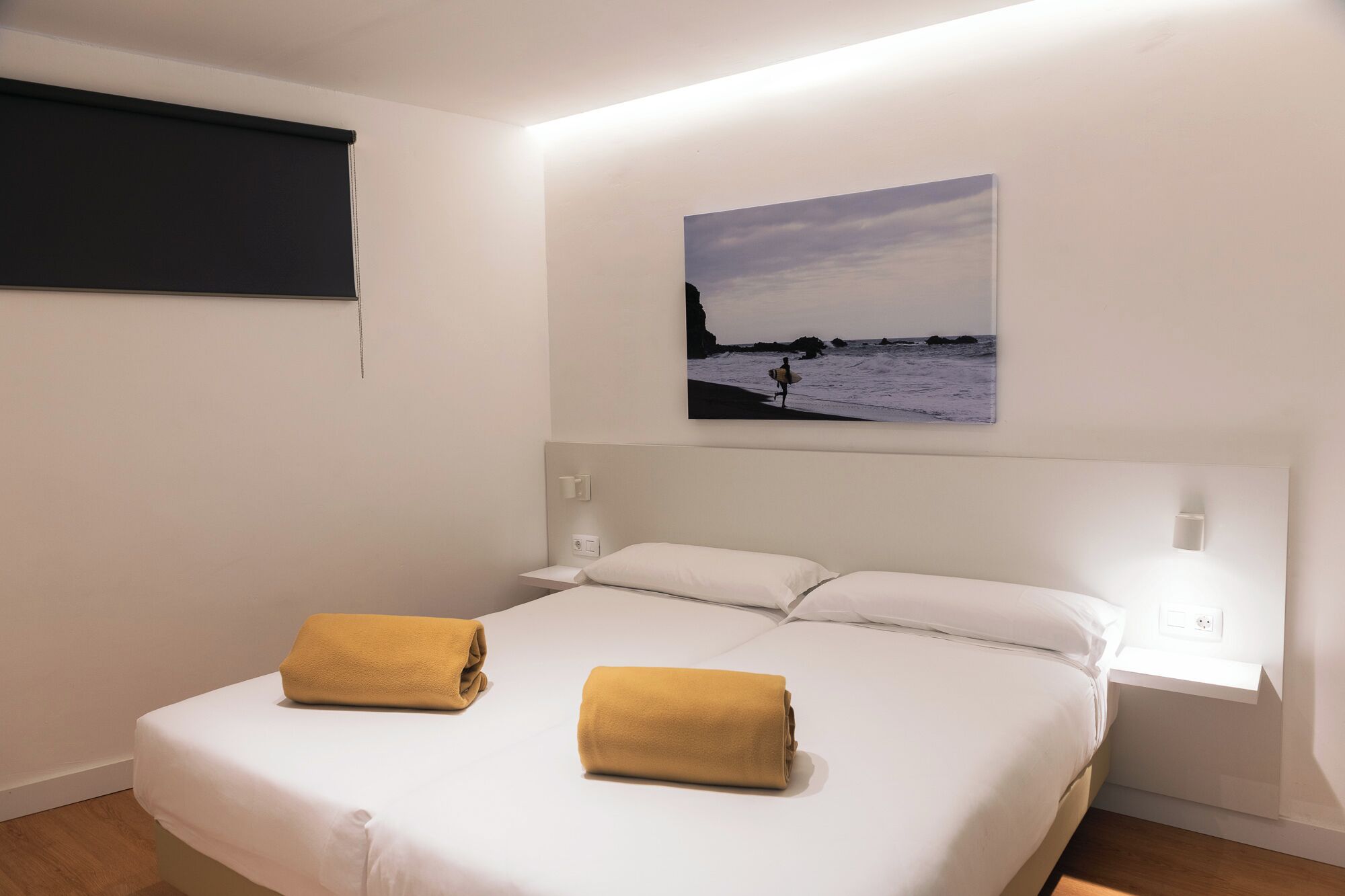 A hotel room with a bed, two towels, a painting of a beach scene, and a window with a view of the sea.