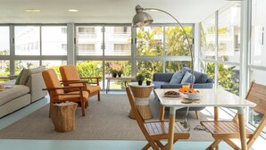 A bright living room with a sofa, chairs, a dining table, and a view of greenery outside. - Route Active Hotel (Los Realejos)