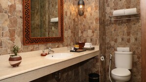 Un baño con pared de piedra, un lavabo, un espejo, una lámpara colgante y un inodoro.