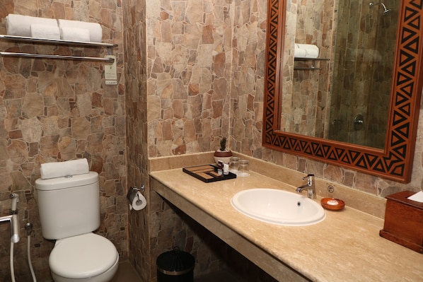Un baño con pared de piedra, un inodoro, un lavabo y un espejo con marco geométrico.