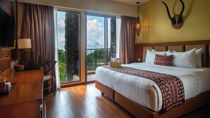 Un dormitorio amplio con una cama grande, un escritorio de madera y un balcón con vistas panorámicas.
