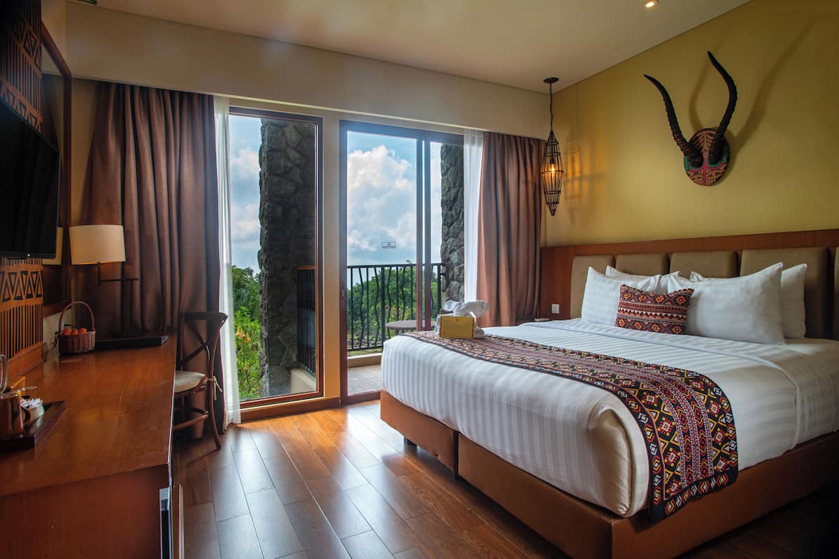 Un dormitorio amplio con una cama grande, un escritorio de madera y un balcón con vistas panorámicas.