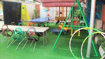 Enjoy outdoor playtime with a table, chairs, ping pong table, and swing set under a shaded area.