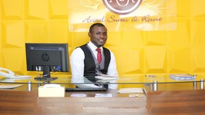 A reception desk with a computer, phone, and various papers. The background features a yellow wall with the logo "ASR" and the text "Avital Suites & Resort". - Avital Suites And Resort (Lagos)