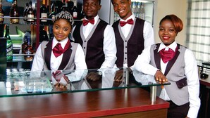 A bar area with a glass counter, bottles, and a computer on a desk. - Avital Suites And Resort (Lagos)