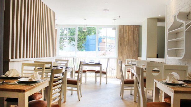 A modern dining area with wooden tables and chairs, large windows, and a brick wall. - Stori Hotel Ambon (Ambon)