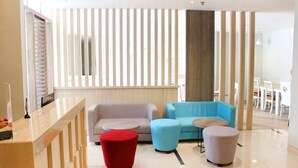A modern lobby with a reception desk, seating area with sofas and ottomans, and a large window with vertical blinds. - Stori Hotel Ambon (Ambon)