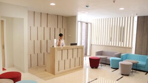 A modern reception area with a wooden reception desk, a red and blue seating area, and a large window with blinds. - Stori Hotel Ambon (Ambon)