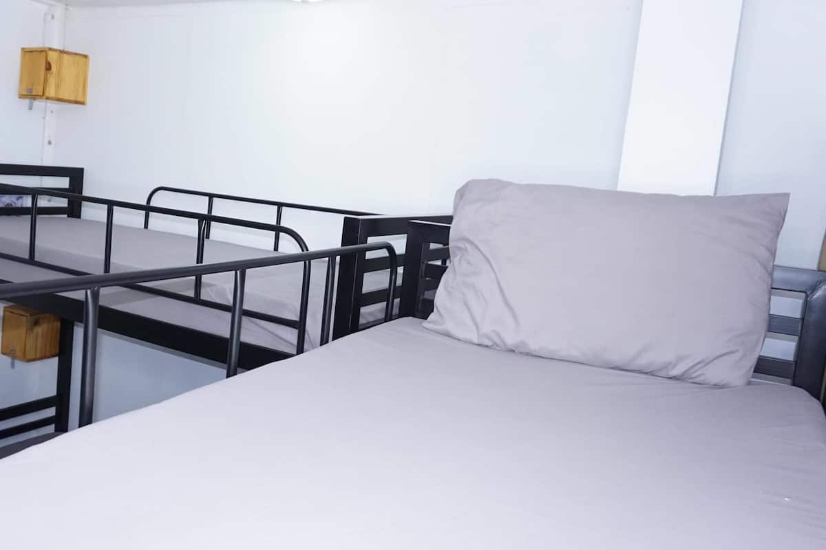 A single bed with a headboard and a pillow, a small table with a chair, a wooden cabinet, and a ceiling light fixture.