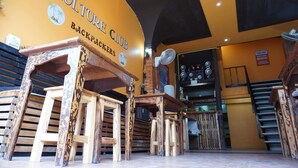 A restaurant interior with a yellow wall, wooden furniture, and a sign reading "Culture Club Backpackers". - Culture Club Backpackers - Hostel (Ko Pha-ngan)