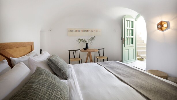 Un dormitorio con una cama, una mesita con sillas, una planta en maceta y una lámpara fijada a la pared.