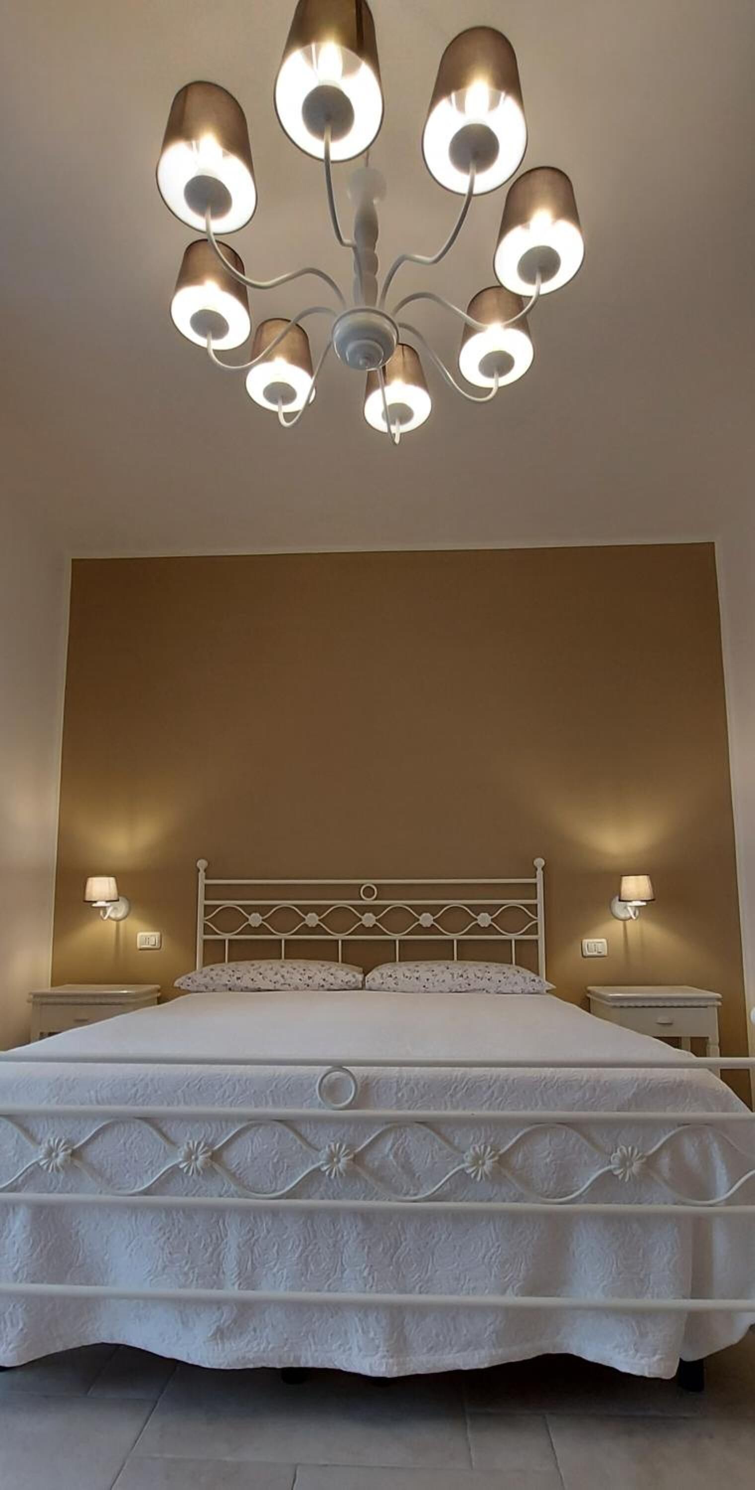 A bedroom with a large bed, a chandelier, and two wall-mounted lamps.