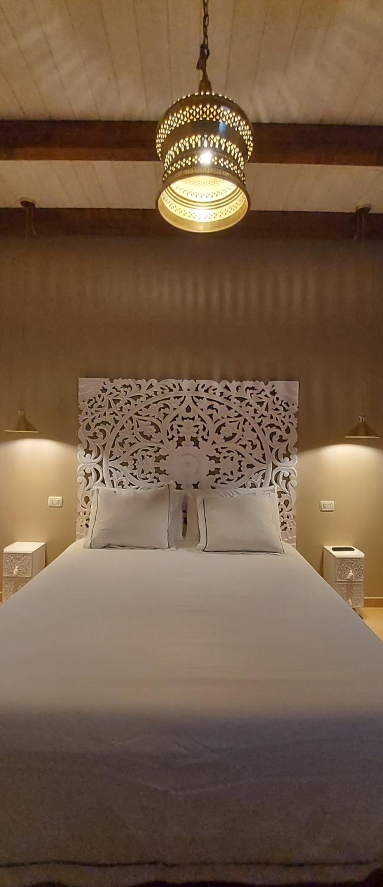 Una cama bien tendida con un cabecero decorativo, una lámpara colgante y lámparas de noche.