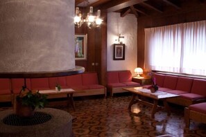 A cozy room with a round table, red sofas, a patterned floor, and a large pillar. - Sport Hotel (Comelico Superiore)