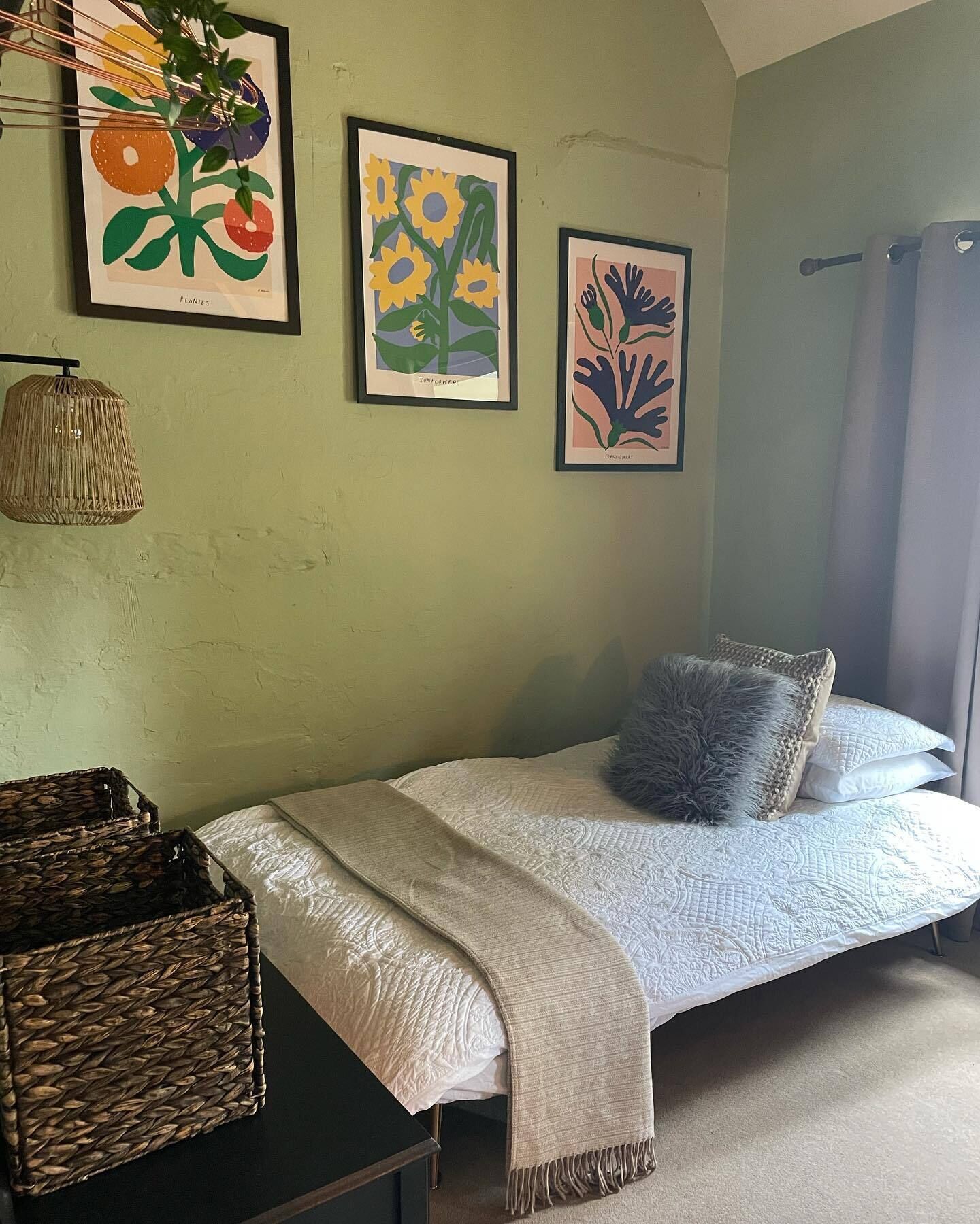 A bedroom with a bed, a woven basket, and three framed artworks on the wall.