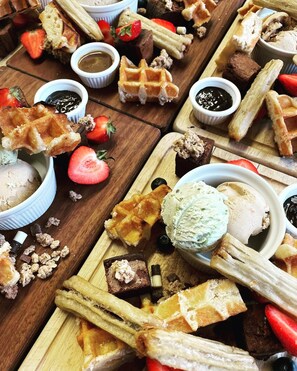 A variety of desserts including waffles, ice cream, and chocolate pieces on a wooden board.