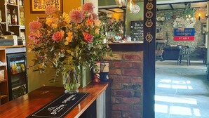 A bar area with a wooden counter, a vase of flowers, hanging light fixtures, and a sign for 'Rode Bird Gardens'.