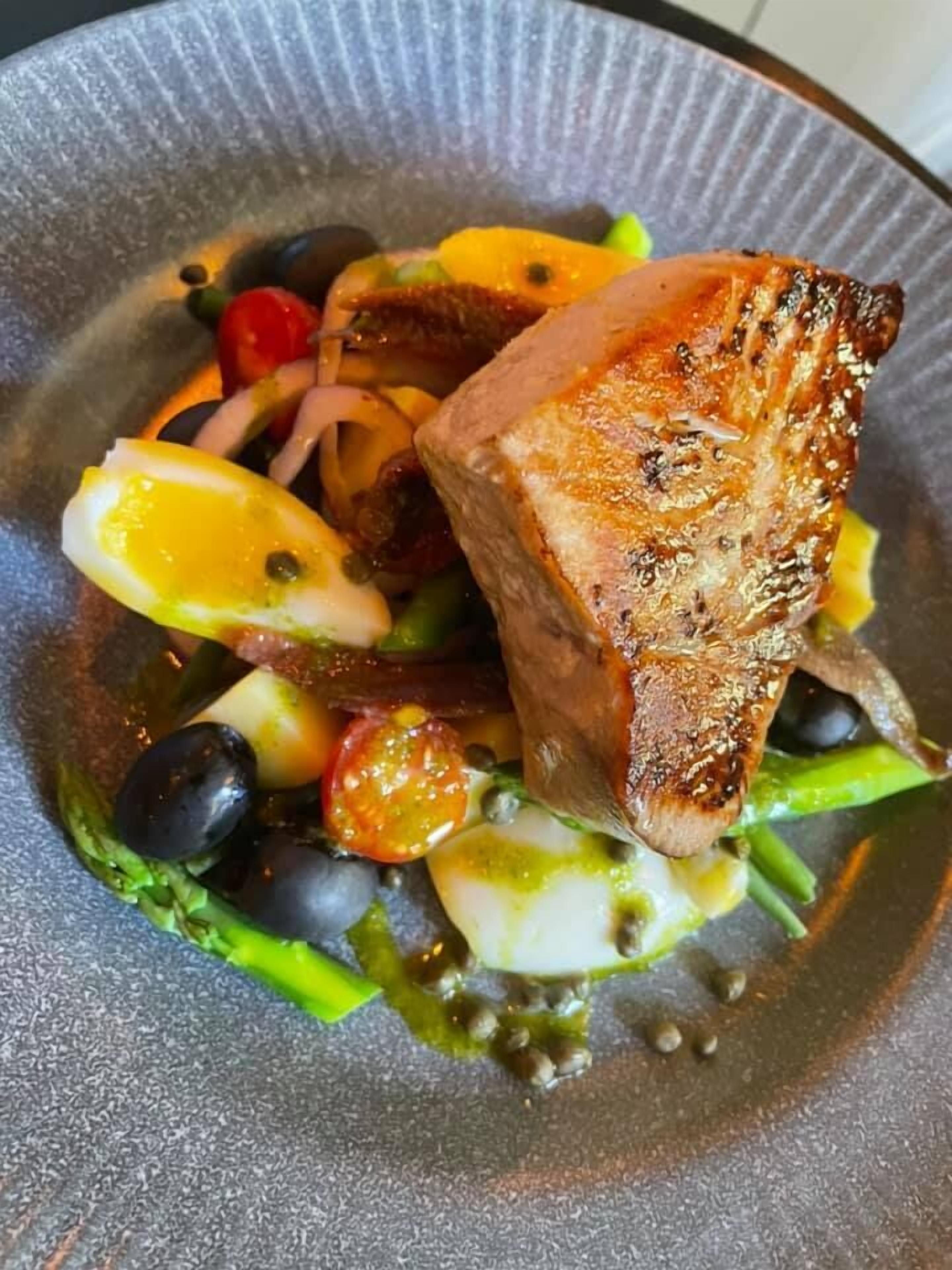 A plate with grilled fish, vegetables, and a lemon wedge.