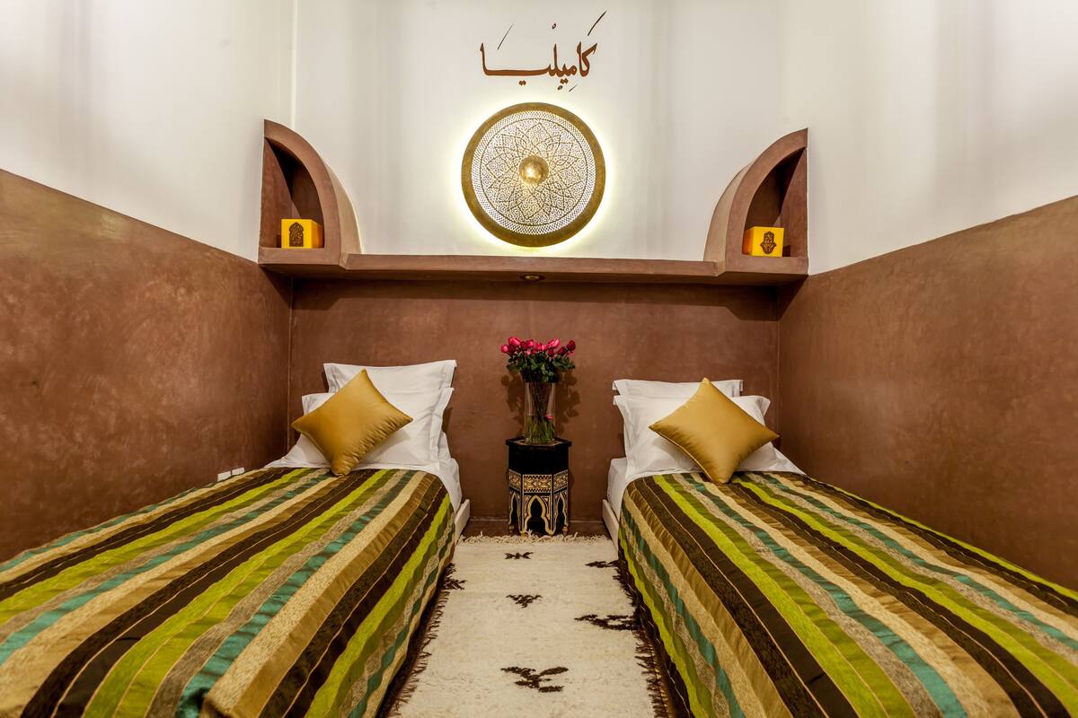 A room with two beds, a decorative wall piece, and a small table with a vase.
