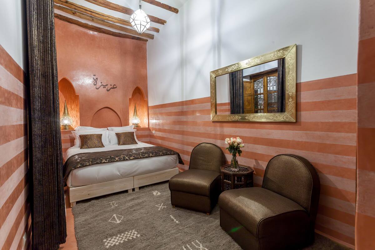 A bedroom with a bed, two chairs, a nightstand, and a mirror.