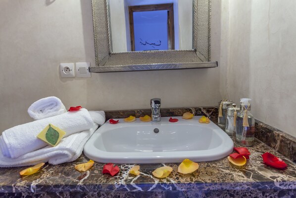 A bathroom with a white sink, marble countertop, rolled towels, and rose petals. - Riad Dar Yema (Marrakech)