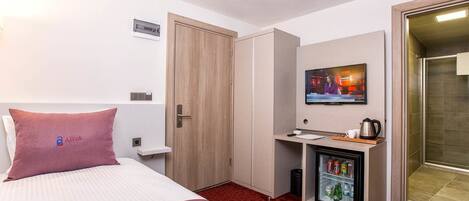 Habitación de hotel con cama, escritorio con televisor, minibar y zona de ducha.