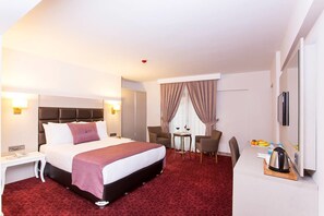 A hotel room with a bed, bedside table, chair, small table with a kettle, and a TV. - Perla Arya Hotel (Izmir)