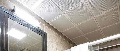 A modern bathroom with a glass shower enclosure, a white sink with a glass top, and a large mirror above the sink.