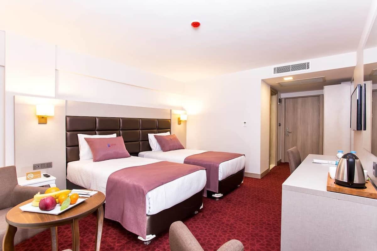 Une chambre d’hôtel avec deux lits, un bureau, une chaise, une petite table avec des fruits et une bouilloire.