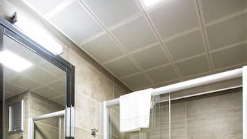 Un baño moderno con ducha envuelta en vidrio, un lavamanos blanco con encimera de cristal y un espejo sobre el lavamanos.