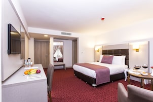 Habitación de hotel con cama, mesita de noche y escritorio con frutas y botellas de agua.
