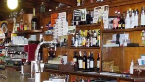 A bar with wooden shelves stocked with various bottles, a coffee machine, and a menu board.