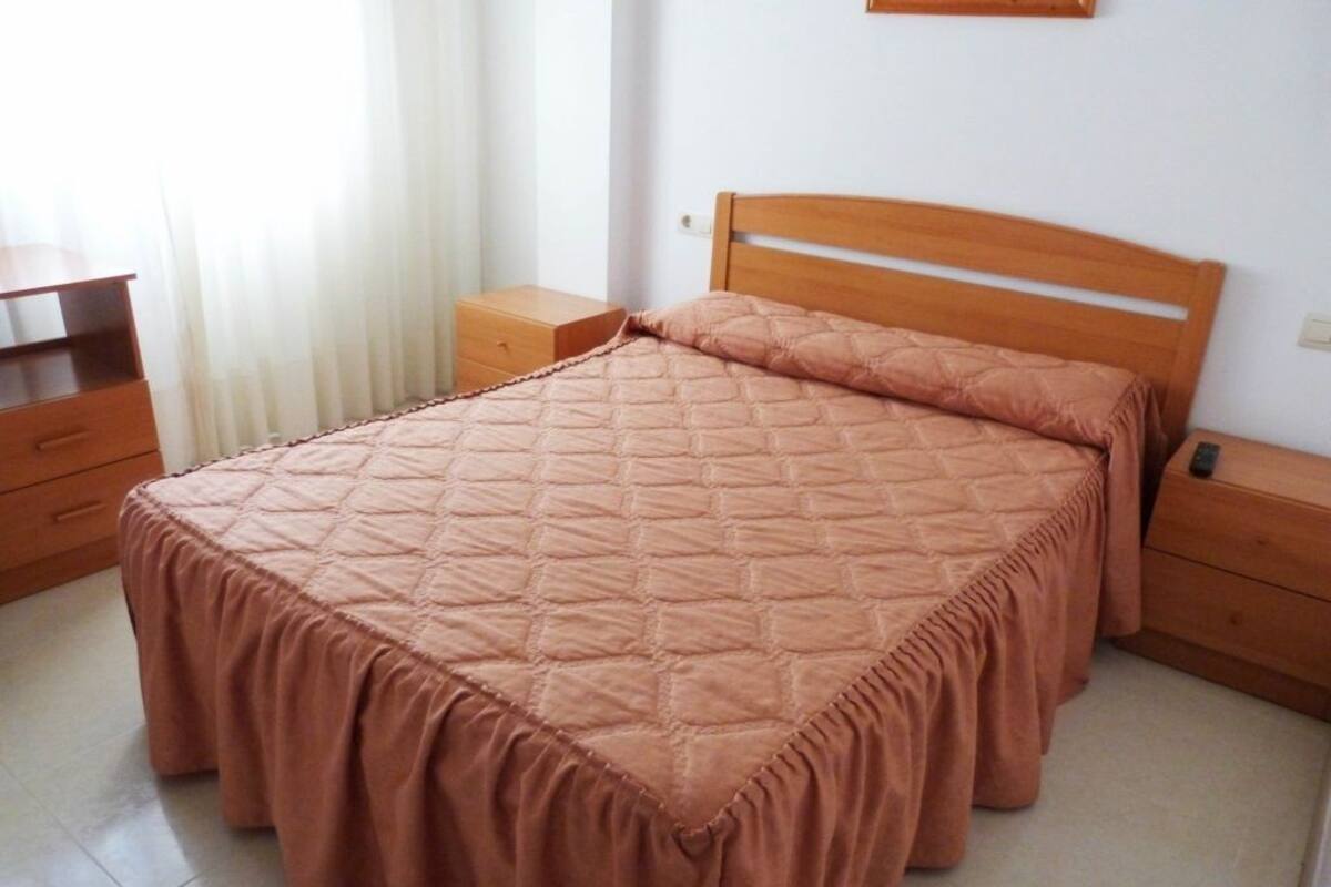 A bedroom with a large bed, wooden headboard, two bedside tables, and a nightstand.