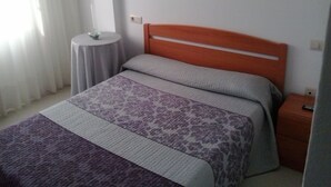 A bedroom with a bed, a round side table, a nightstand, and a wall-mounted light switch.