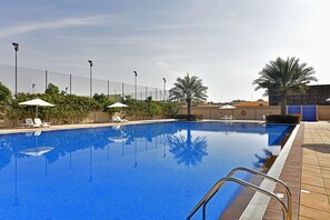 A swimming pool with clear blue water, surrounded by lounge chairs and umbrellas, and a fence in the background. - Jannah Hotel Apartments & Villas (Ras Al Khaimah)