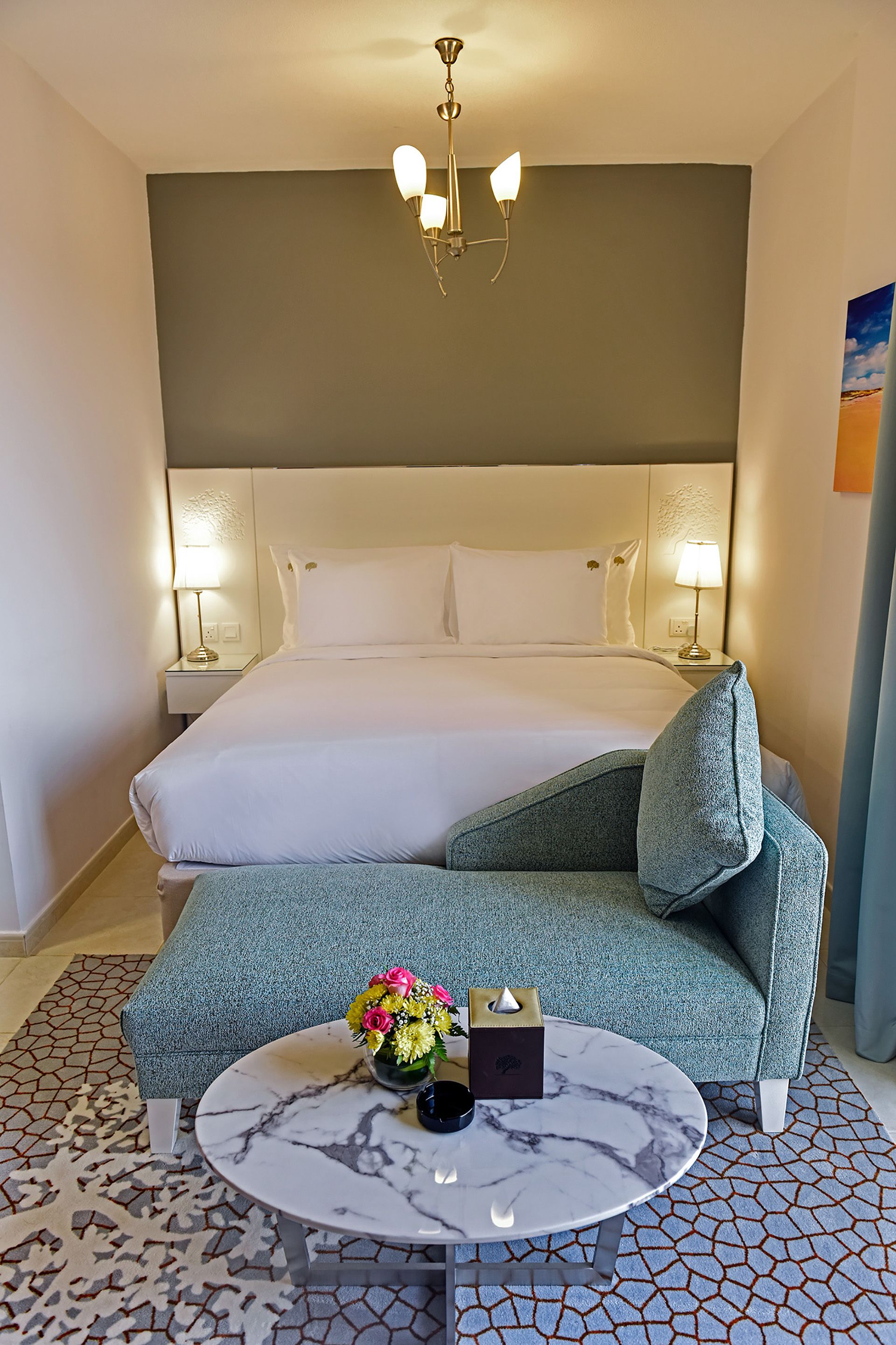 Una habitación de hotel con una cama grande, un sofá verde, una mesa de centro de mármol redonda y una araña.