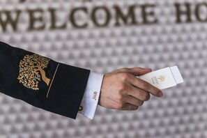 A hand holding a white card with a logo, in front of a background with a "WELCOME HOME" sign. - Jannah Hotel Apartments & Villas (Ras Al Khaimah)