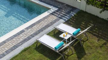 A poolside area with two sun loungers, a small table with a towel, and a glass of orange juice.